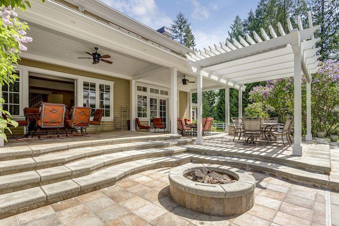 Lovely outdoor deck patio space with white pergola, fire pit in the backyard of a luxury house.